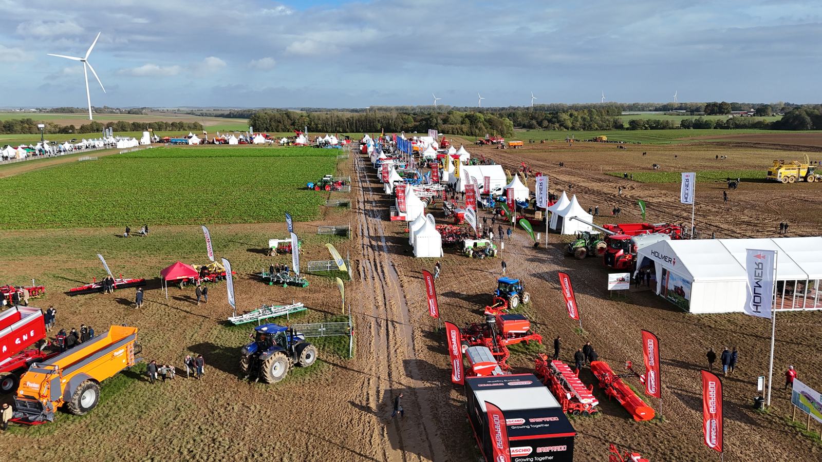 Aerial view of an open-field agricultural show with stands, tents and machinery